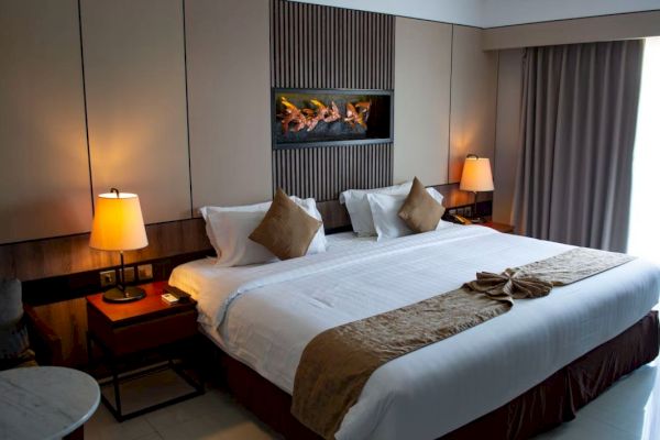 A neatly arranged hotel room with a large bed, two lamps, and curtains. Wall decor and a seating area provide a warm, inviting ambiance.