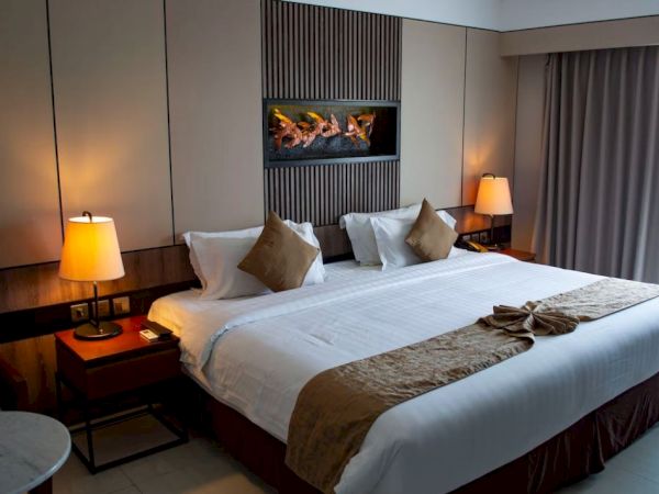 A neatly arranged hotel room with a large bed, two lamps, and curtains. Wall decor and a seating area provide a warm, inviting ambiance.