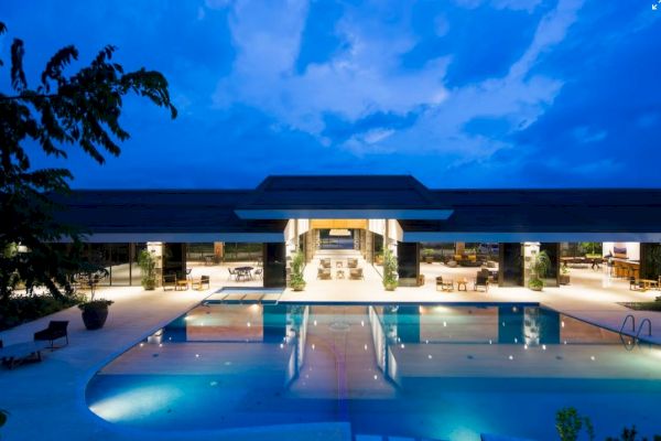 A luxurious building at night with a large illuminated pool, surrounded by seating areas and greenery under a deep blue sky.