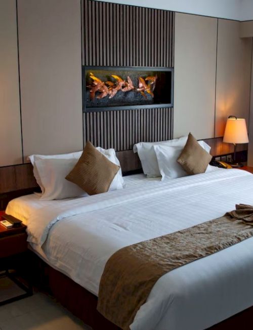 A cozy hotel room with a large bed, decorative pillows, bedside lamps, and a wall feature, creating a warm ambiance.