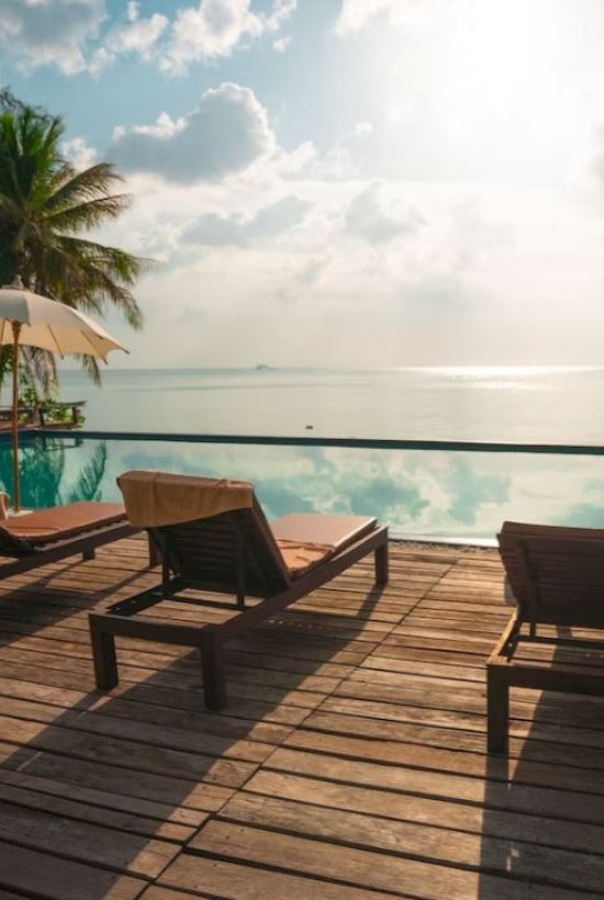 A serene poolside view with lounge chairs, umbrellas, and a tranquil ocean backdrop under a partly cloudy sky.