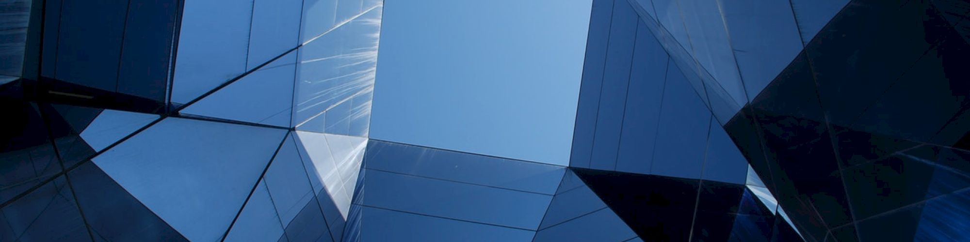 Geometric architecture with mirrored surfaces forms a skyward perspective, featuring reflections and angular designs.