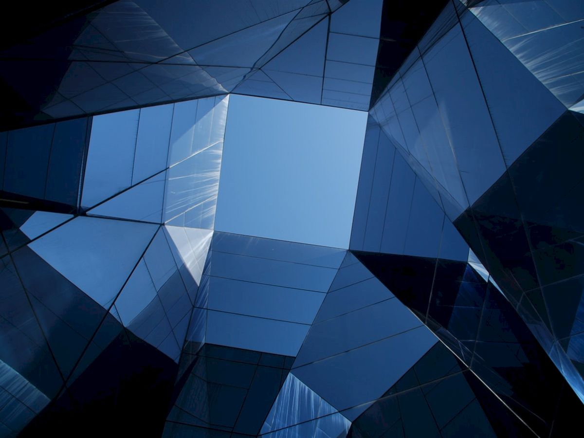 The image shows a geometric arrangement of reflective blue glass surfaces creating an abstract architectural pattern against the sky.