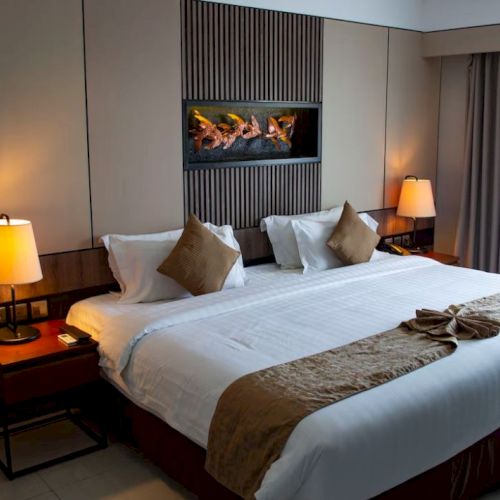 A hotel room with a large bed, two bedside lamps, and decorative pillows on a brown and white color scheme.