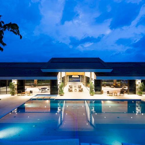 The image shows an illuminated building with a large swimming pool in front, set against a stunning evening sky.