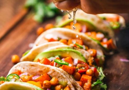 Tacos filled with chickpeas, diced vegetables, and garnished with avocado and cilantro, being sprinkled with lime juice.