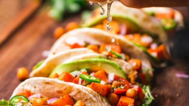 Tacos filled with chickpeas, diced vegetables, and garnished with avocado and cilantro, being sprinkled with lime juice.