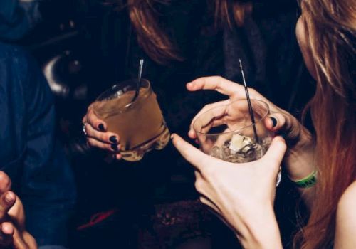 People are enjoying a night out, holding drinks and engaging in lively conversation, with visible expressions of laughter and fun.