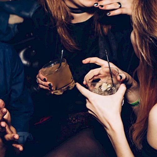 People are enjoying a night out, holding drinks and engaging in lively conversation, with visible expressions of laughter and fun.