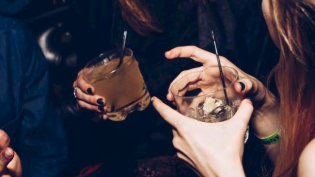 People are enjoying a night out, holding drinks and engaging in lively conversation, with visible expressions of laughter and fun.