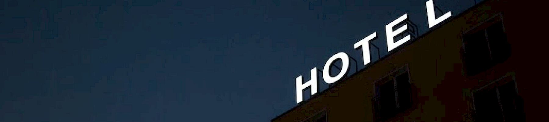 The image shows a building at night with an illuminated sign saying "HOTEL," but the letter "H" is not lit, making it read "OTEL."