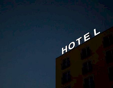 The image shows a building at night with an illuminated sign saying "HOTEL," but the letter "H" is not lit, making it read "OTEL."