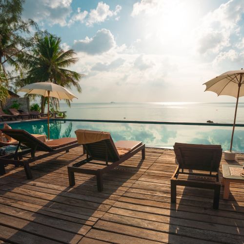 A tranquil beachfront scene with lounge chairs, umbrellas, and a calm ocean view, under a bright sky with scattered clouds.