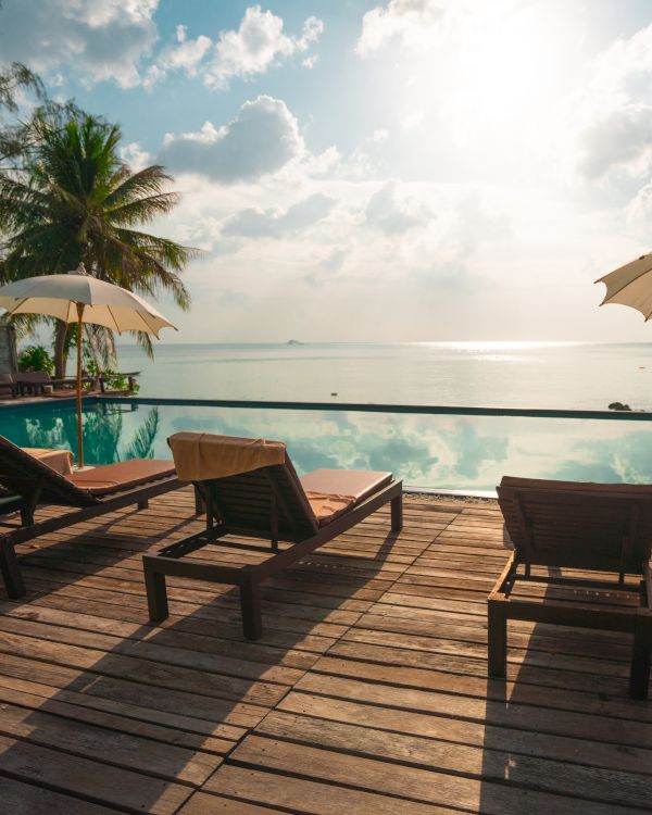 A tranquil beachfront scene with lounge chairs, umbrellas, and a calm ocean view, under a bright sky with scattered clouds.