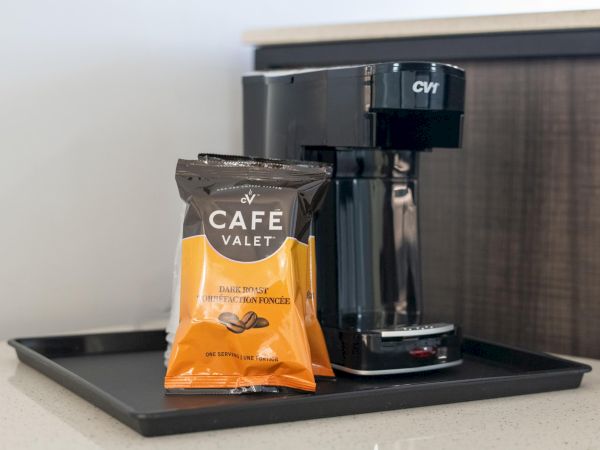 The image shows a coffee maker on a tray with a packet of Café Valet coffee placed in front of it on a countertop.
