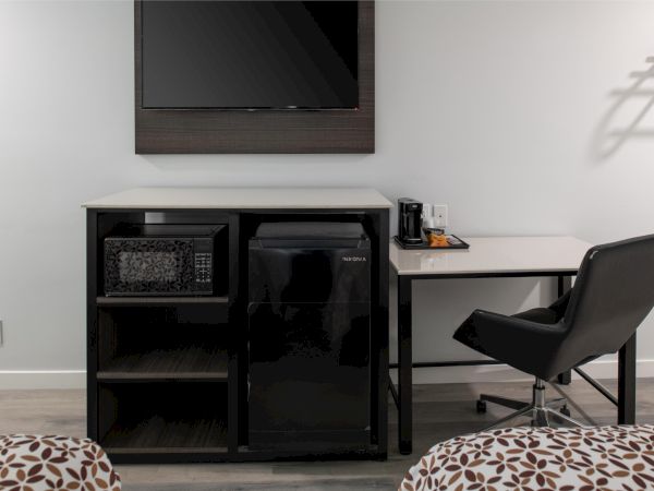 The image shows a hotel room setup with a TV, microwave, mini-fridge, desk, coffee maker, chair, and bed corners in view.