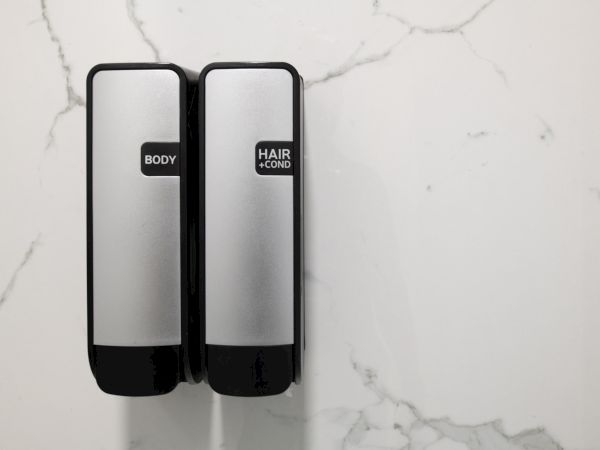 Two wall-mounted dispensers labeled "Body" and "Hair + Cond." on a marble background.