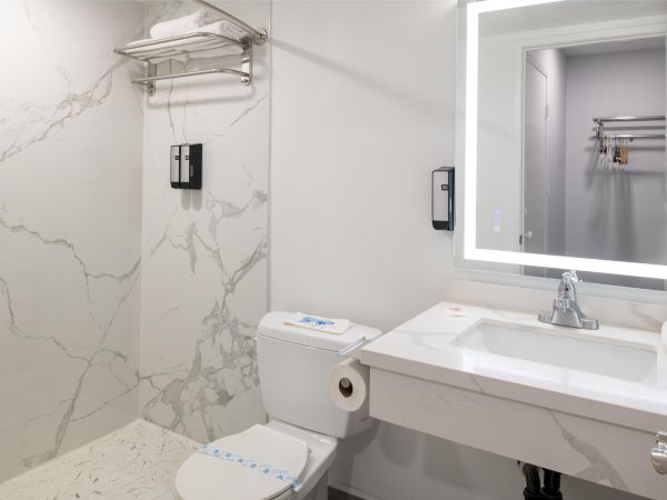 A clean, modern bathroom with a large mirror, sink, toilet, shower area, and towel rack on a wall with a marble finish.
