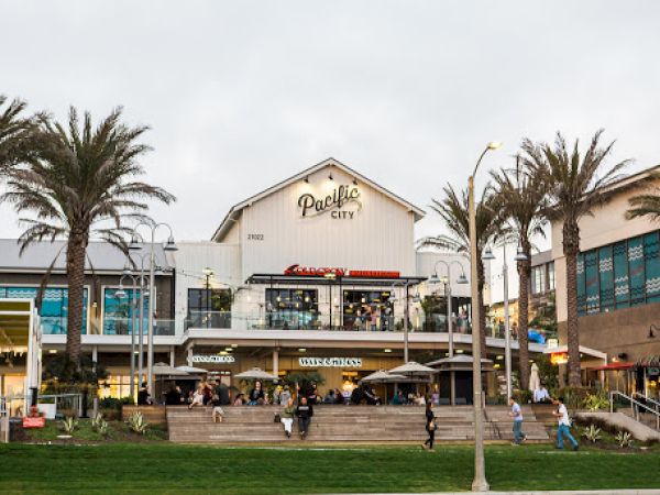 A lively shopping center with palm trees, featuring "Pacific City" signage, outdoor seating, and people walking around.