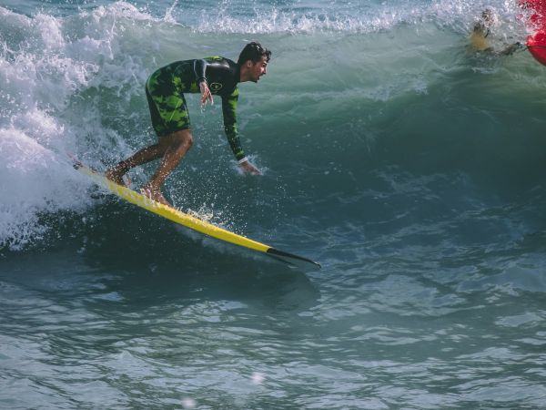 A person surfing on a wave with a yellow surfboard, wearing a wetsuit, surrounded by ocean water.