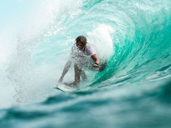 A surfer rides inside a turquoise wave, skillfully maneuvering through the tunnel of water.