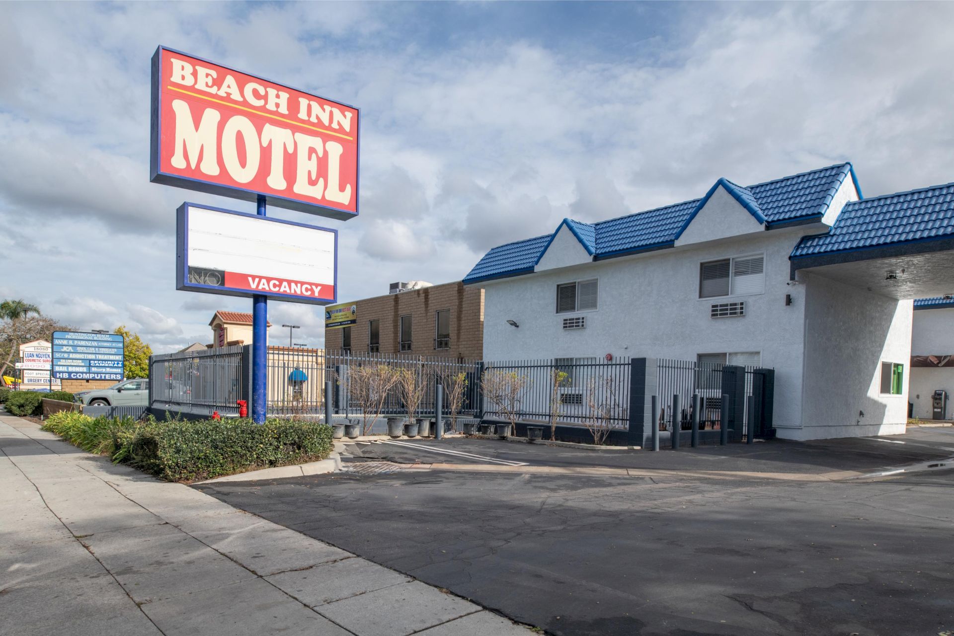 A motel with a sign reading "Beach Inn Motel" and "Vacancy" is shown, with a white building and blue roof next to a parking area.