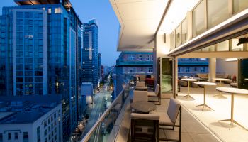 A modern cityscape view with tall buildings and a stylish balcony featuring outdoor seating at dusk.