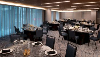 The image shows an elegantly set dining area with round tables, chairs, and tableware, accented by soft lighting and decorative flowers.