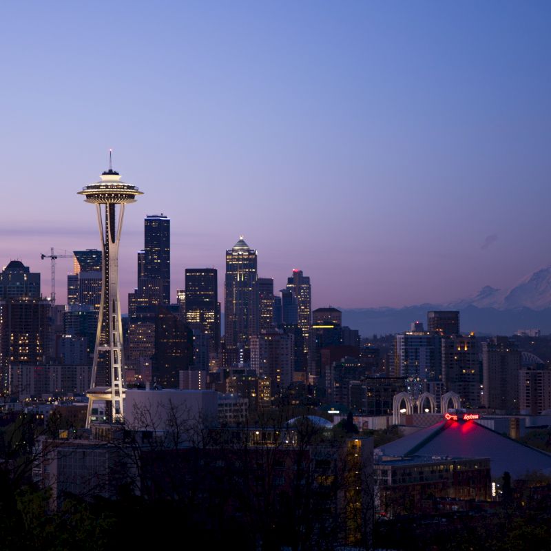 The image shows the Seattle skyline at dusk with the Space Needle, skyscrapers, and Mount Rainier in the background.