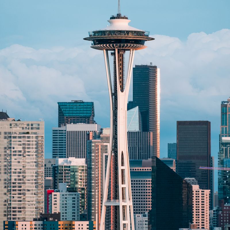 The image shows the Space Needle, a prominent tower in Seattle, with the city skyline and various buildings in the background.