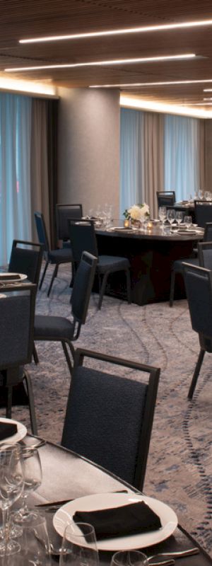 The image shows an elegantly set dining room with round tables, chairs, and soft lighting, ideal for a formal event or banquet.