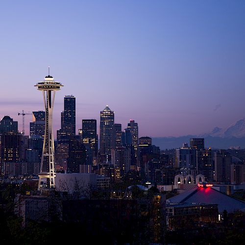 Seattle skyline at dusk, featuring the Space Needle with Mount Rainier in the background under a clear sky.