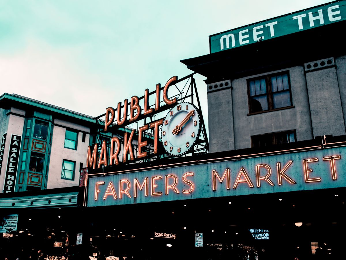 A vibrant sign reading "Public Market" and "Farmers Market" with a large clock is displayed on a building.